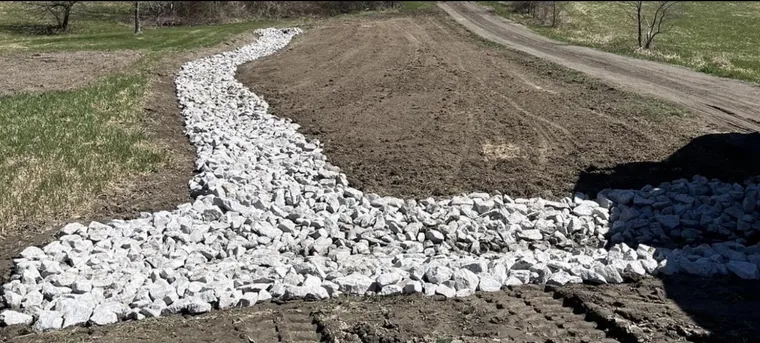 Stone-lined swale carrying runoff clear of the drive